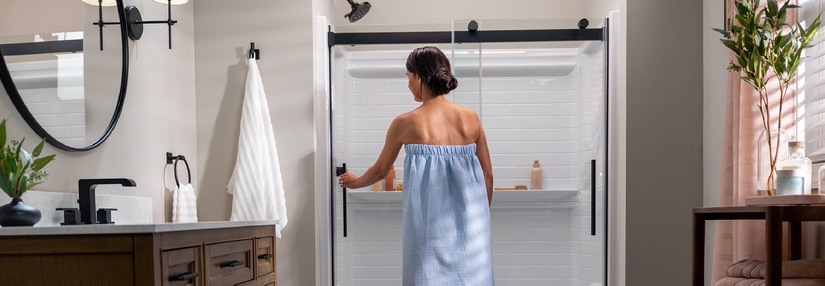 Woman in a blue towel standing in a bathroom with a glass shower door.