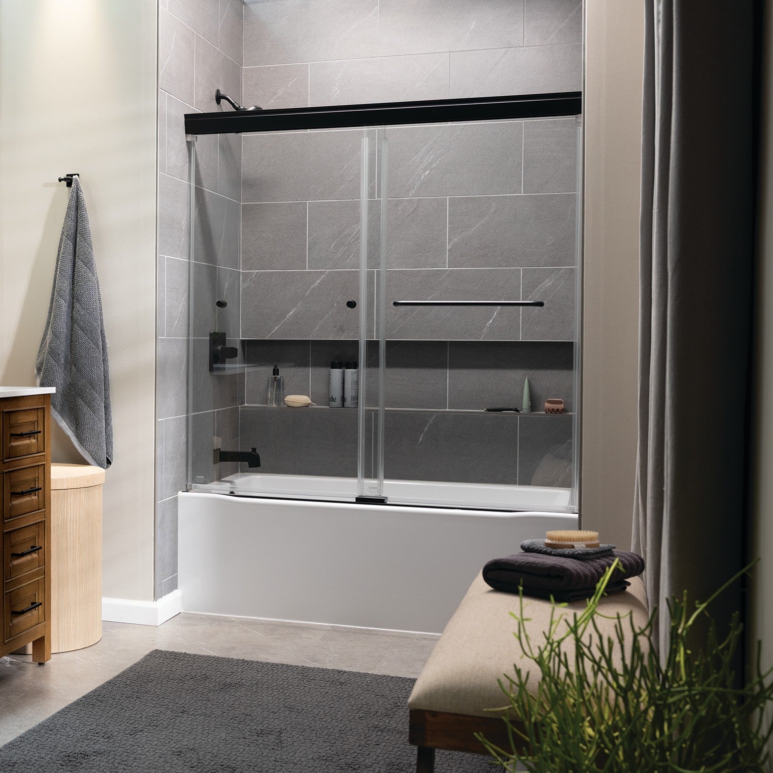 Bathroom with a bathtub and shower enclosure, featuring a wooden cabinet and gray tiles.