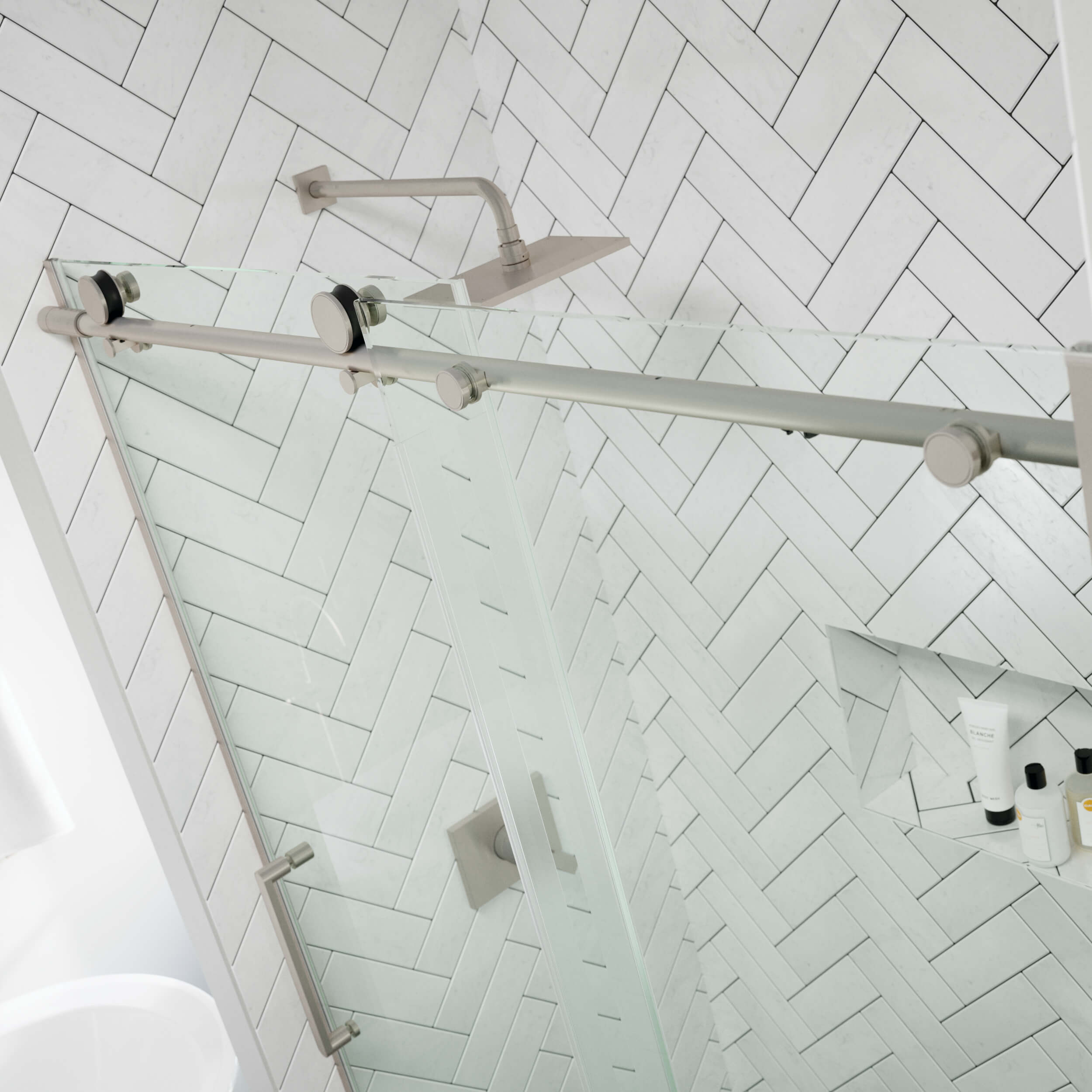 Glass shower enclosure with metal fixtures against a white tiled wall.
