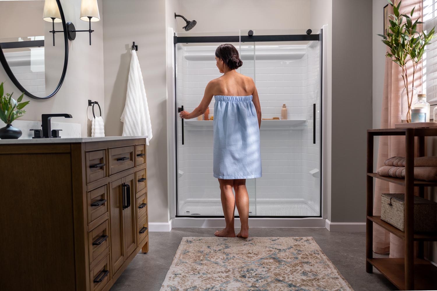 Woman in a blue towel standing in front of a glass shower door in a bathroom.
